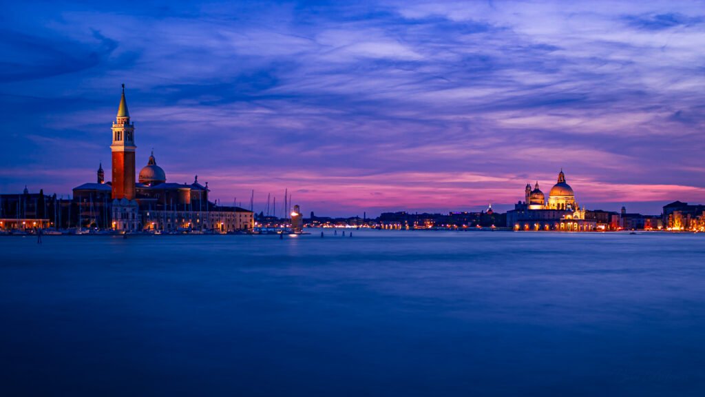 San Giorgio Maggiore island in Venice silhouetted at twilight, with a dramatic pink, blue, and golden sky above the lagoon.