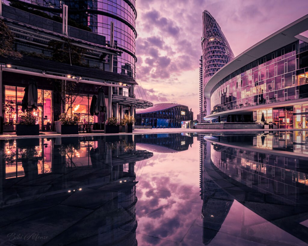 Pink sunrise illuminating Piazza Gae Aulenti in Milan, with reflections of modern architecture against a pink and gold sky.