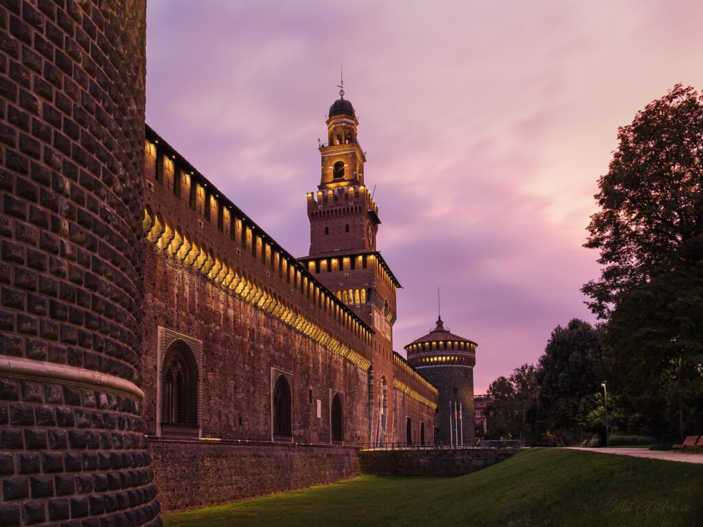Long exposure capturing a soft pink sunrise over Castello Sforzesco in Milan, Italy, with gentle light illuminating the historic architecture.